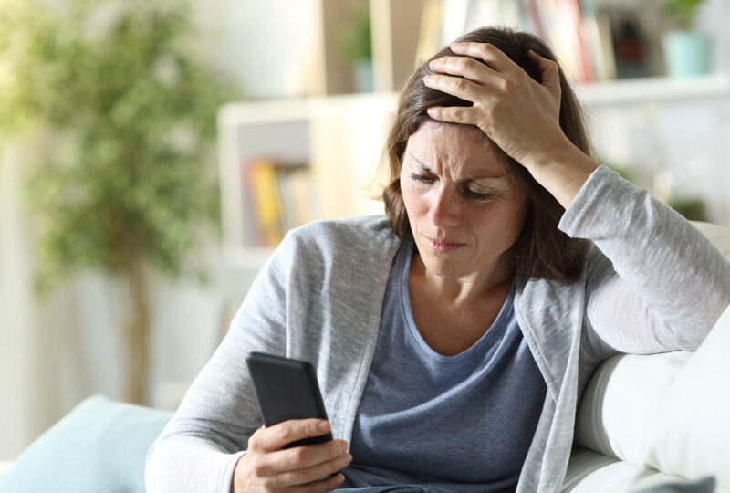 upset woman looking at phone in hand