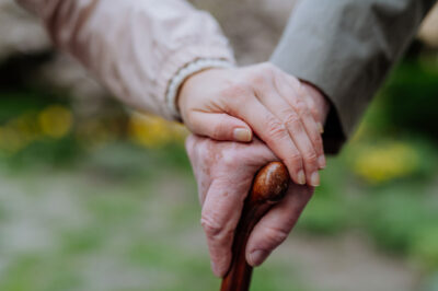 Close-up of adult daughter holding her senior father's hand outdoors on a walk in park