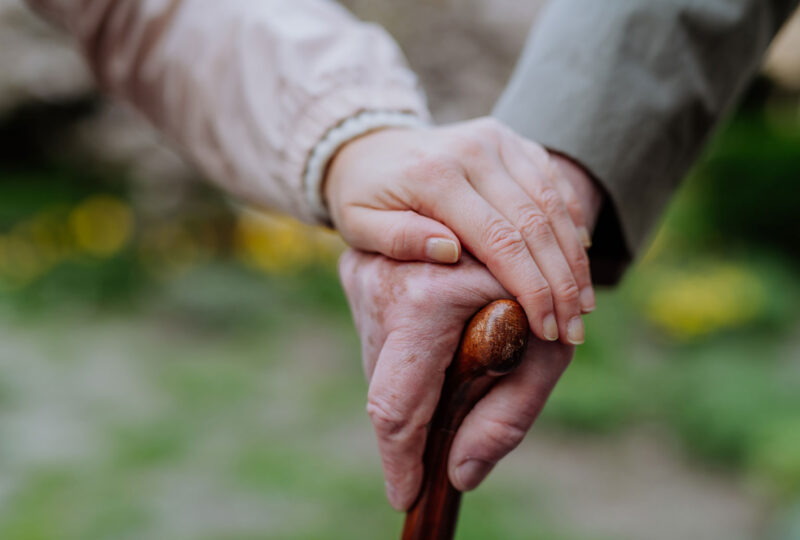 Close-up of adult daughter holding her senior father's hand outdoors on a walk in park