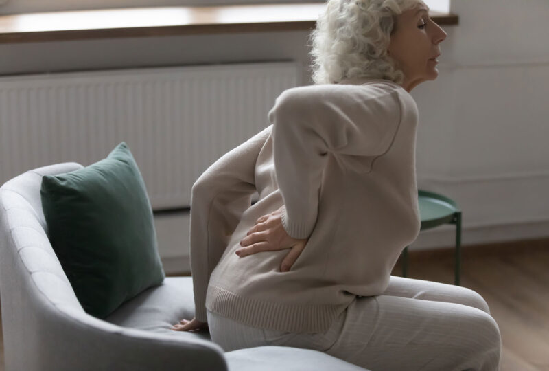 senior woman standing up from chair holding back in pain