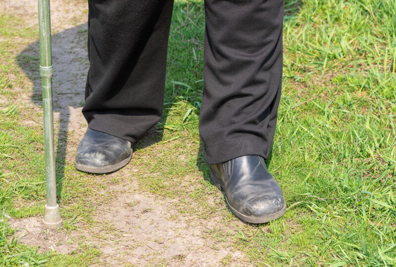 Man with walking stick wearing old scratched shoes walking on a path