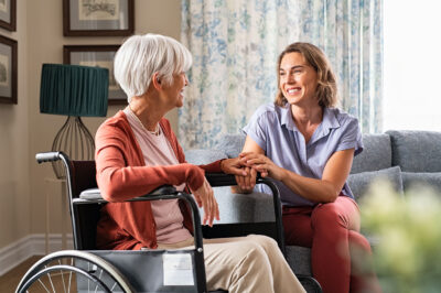 at home care worker holding hand of senior woman in wheelchair
