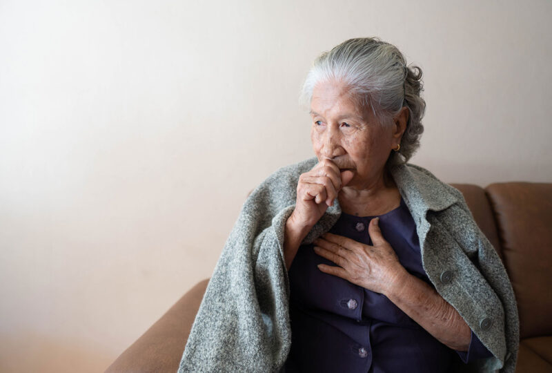 older woman coughing with a blanket around her shoulders