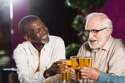 happy senior multiethnic friends clinking beer glasses while spending time in pub