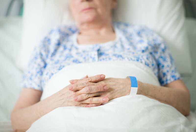 blurry image of senior woman in hospital bed with her hands folded