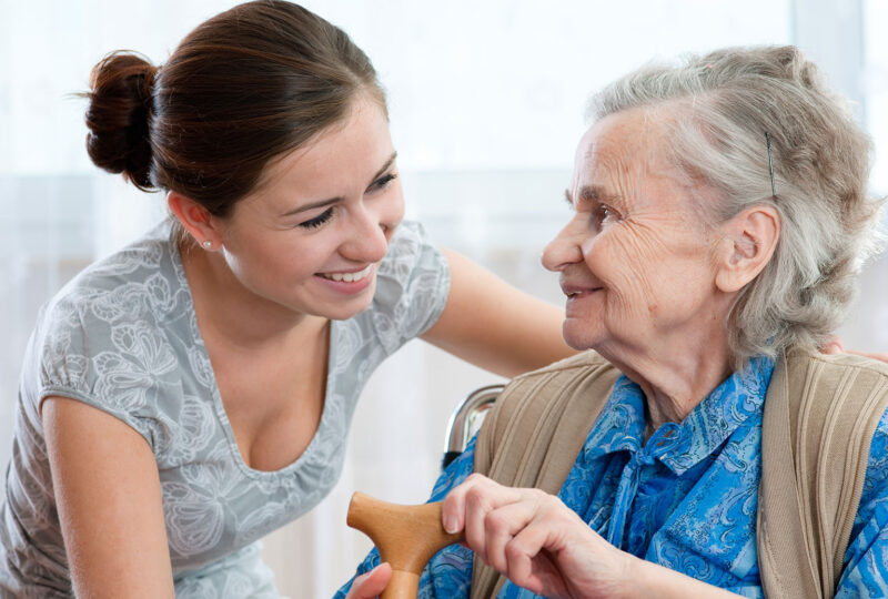 senior woman holding cane smiling at her caregiver