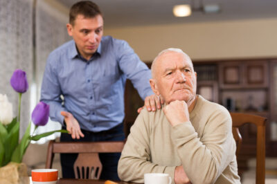 man sitting at table with disgruntled adult son standing behind