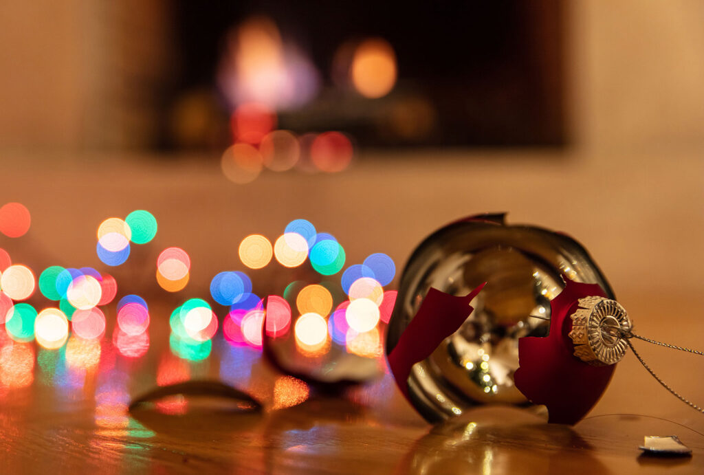 Christmas ornament broken. Xmas holiday decoration, lights glowing, blur burning fireplace background, reflections on the wood floor