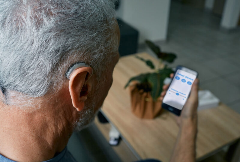 senior man with hearing aid looking at a smartphone