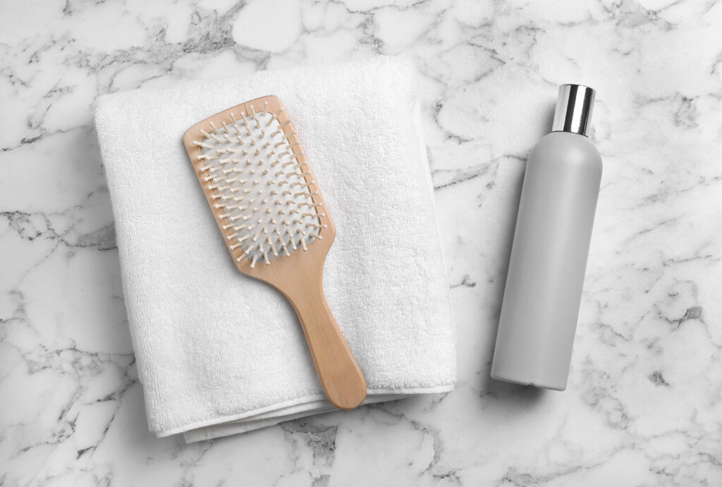 Towel, hair brush and shampoo on marble background, top view