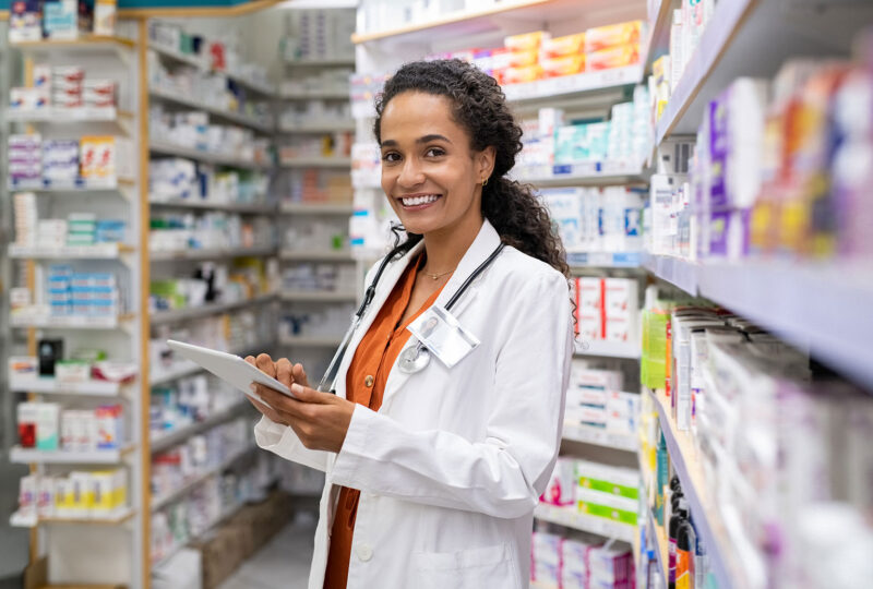 Happy friendly pharmacist doing inventory in a provided and modern pharmacy