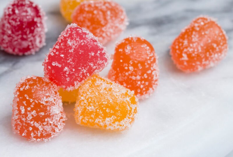 Closeup of gummy candy gumdrops in red, yellow, and orange on a white marble surface. Vitamin supplement