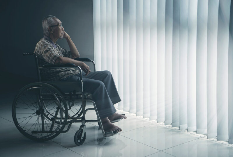older man in wheelchair looking out a window