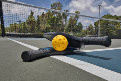 Closeup of a pickleball and paddles on an empty court under sunny skies
