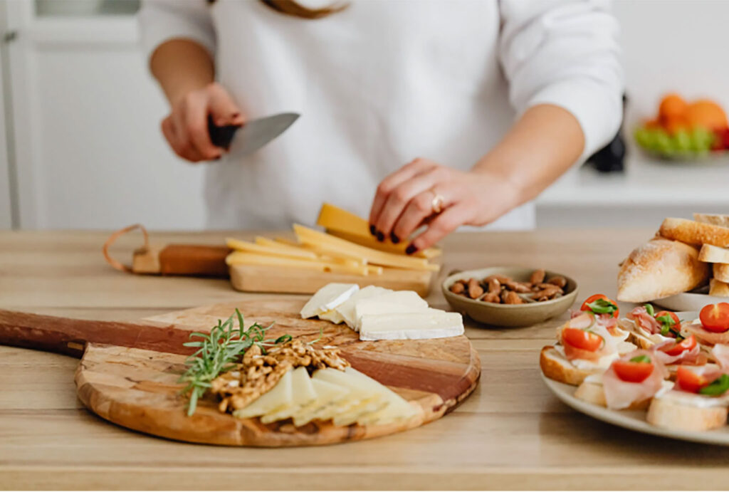 person slicing up cheese to prepare a charcuterie board in the foreground