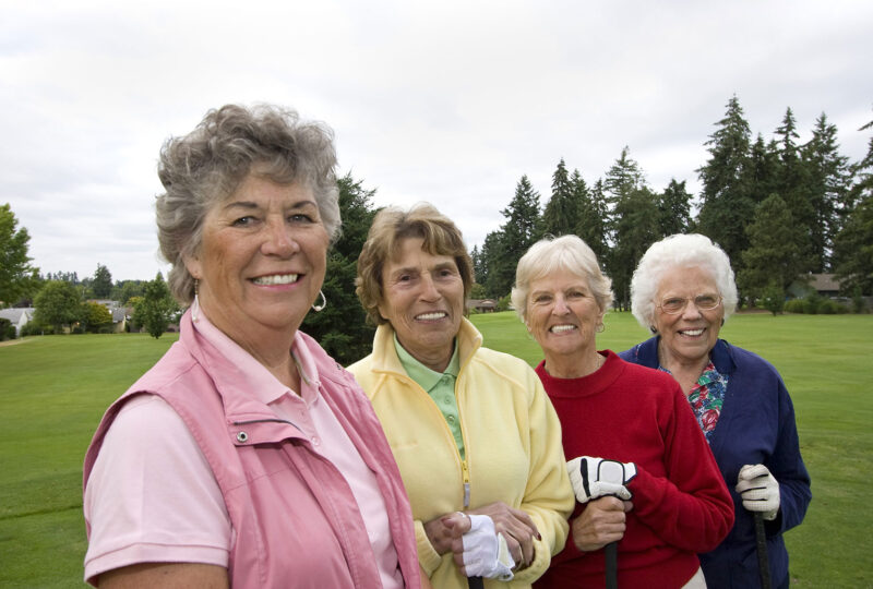 Four smiling, senior women carrying golf clubs.