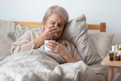 Older woman sick in bed blowing her nose